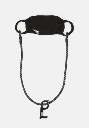 Sort stofmaske med elastiske øre-loop og en aftagelig sort-hvid prikket rem med en clip til sikker fastgørelse.