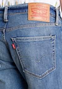 Vaaleansiniset farkut, joissa on nahkainen merkki, jossa lukee "Levi Strauss & Co.", ja takataskussa erottuva V-muotoinen ommel.