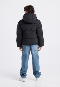 Black puffer jacket with a hood, featuring a quilted design. Worn with light blue baggy jeans and white sneakers.