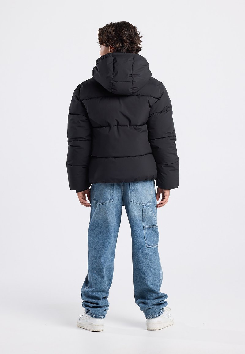 Black puffer jacket with a hood, featuring a quilted design. Worn with light blue baggy jeans and white sneakers.