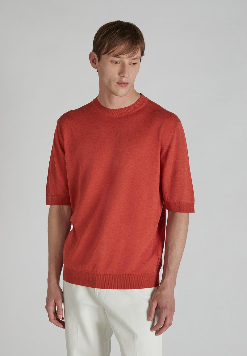 Sweter z krótkim rękawem i okrągłym dekoltem w bogatym czerwonym odcieniu, wykonany z miękkiego materiału z prążkowanymi mankietami i dołem, z bocznymi rozci ęciami dla większej swobody ruchów.