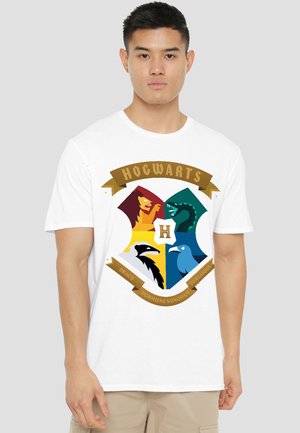 Young man wearing a white t-shirt with a colorful Hogwarts crest featuring a lion, snake, badger, and eagle on the front.