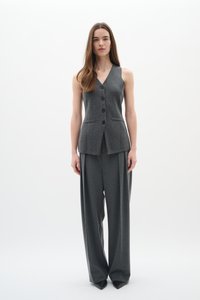 Gilet grigio senza maniche con bottoni e tasche laterali abbinato a pantaloni grigi larghi, caratterizzati da un design su misura e una texture liscia.