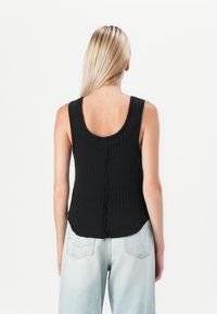Svart ribbet tanktopp med rundet halslinning og en teksturert søm nedover ryggen, kombinert med lyseblå høytlivsjeans.