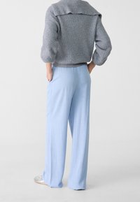 Un pantalon large bleu clair avec une finition lisse et texturée, associé à un pull en laine gris avec un col rabattu et des manches trois-quarts.