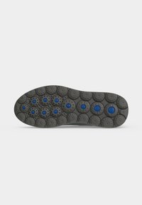 Semelle de chaussure en caoutchouc avec motifs de bande de roulement circulaires comprenant plusieurs inserts ronds bleus pour la traction et l'adhérence sur un fond clair.