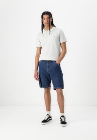 Grå kortærmet T-shirt med et lille logo, parret med blå denimshorts og sorte sneakers med hvide accenter. Renset, afslappet look.