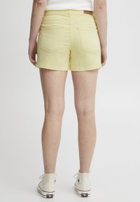 Shorts de mezclilla amarillos con un corte recto, dobladillo deshilachado y dos bolsillos traseros; combinados con zapatillas altas blancas.