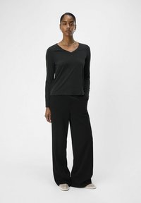 Schwarzes Langarm-V-Ausschnitt-Oberteil, kombiniert mit weiten schwarzen Hosen. Glatte Stofftextur, schlichtes Design, lockere Passform und ohne sichtbare Muster.