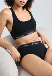 Fekete pamut sportmelltartó és alsónemű szett Calvin Klein logóval az elasztikus pántokon, egyszerű, testhez simuló dizájnnal és sima textúrával.