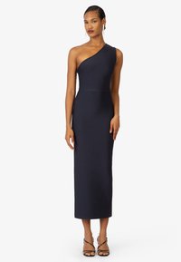 Robe midi bleu marine à une épaule en tissu extensible, silhouette ajustée, épousant le corps jusqu'à la cheville, assortie à des talons noirs à lanières.