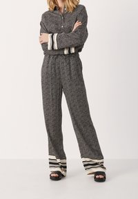 Zwart-wit houndstooth patroonoutfit met een collared button-up blouse en elastische taillebroek, met gestreepte manchetten en een wijduitlopende pasvorm.