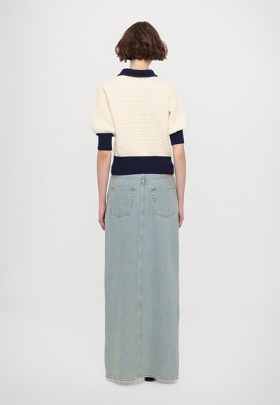 Pull en tricot crème et marine avec un corps texturé et des poignets côtelés ; associé à une longue jupe en denim bleu clair à coupe droite.