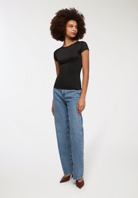 Top aderente nero a maniche corte abbinato a jeans a vita alta azzurri con gamba dritta e tacchi marroni con punta a punta. Tessuto dalla texture liscia.