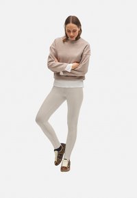 Leggings beige claro con detalles en la costura lateral, combinados con un sudadera topo de cuello alto y una camisa blanca superpuesta por debajo; zapatillas de deporte con estampado animal.