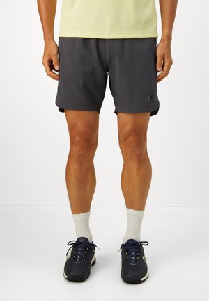 Mann iført svarte treningsshorts, hvite ankelsokker og svarte sportssko, stående mot en ensfarget hvit bakgrunn.