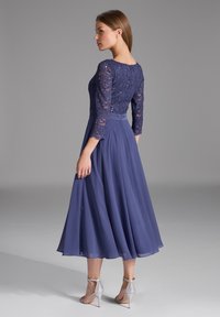 Robe en dentelle marine avec des manches trois-quarts, jupe évasée et accents en perles. Tissu fluide et long avec une texture lisse. Talons à bride cheville argentés.