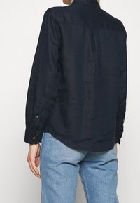 Camicia a maniche lunghe blu navy realizzata in tessuto leggero, con colletto, polsini con bottone e orlo curvo.
