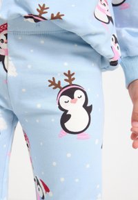 Blue pajama pants featuring a playful penguin print with snowflakes, reindeer antlers, and pink accents; made of soft fabric with a smooth texture.