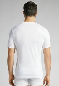 Hvid bomulds t-shirt med korte ærmer og rund hals. Glat overflade, tætsiddende design og ærmer i mellem længde. Bæres med matchende shorts.