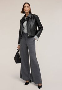 Giacca da moto nera in pelle con accessori dorati, maglione grigio a maglia, pantaloni larghi grigi, borsa nera e décolleté nere con punta.