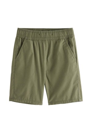 Ung dreng stående iført beige kortærmet skjorte med palmeprint, olivengrønne shorts, cremefarvede sokker og tan sneakers.