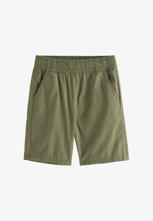 Ung dreng stående iført beige kortærmet skjorte med palmeprint, olivengrønne shorts, cremefarvede sokker og tan sneakers.