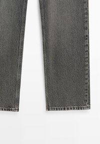 Jambes de jean en denim gris à coupe droite avec coutures visibles sur un fond blanc, montrant la texture du tissu et les ourlets.