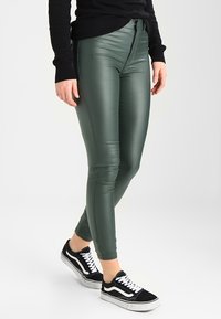 Gröna faux läder leggings med en figurnära design, hög midja, och kontrasterande svarta sneakers med vita ränder.
