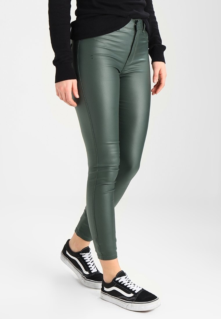 Gröna faux läder leggings med en figurnära design, hög midja, och kontrasterande svarta sneakers med vita ränder.