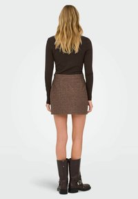 Donkere tweed minirok met een rechte snit, textuur op het oppervlak en een tailleband. Draag het met kniehoge bruine leren laarzen.