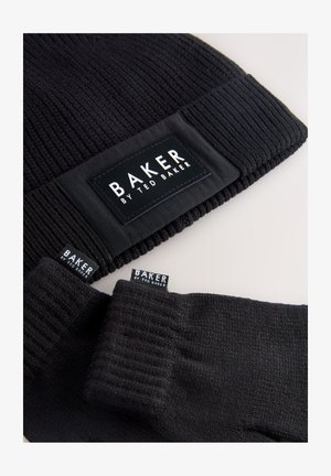 Mustast kudumist mõts koos lamedaplekilise sildiga, kus on kirjas "BAKER BY TED BAKER." Komplekti kuuluvad ka sobivad mustad kudumkõrme, millel on sarnased brändisildid.