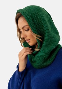 Zielony, dzianinowy kaptur z fakturowanym wzorem, opadający na ramiona, w zestawieniu z niebieskim swetrem. Materiał wydaje się gruby i ciepły.