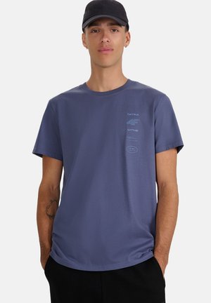 Krótki rękaw, koszulka z okrągłym dekoltem w kolorze granatowym z bawełny, z nadrukami logo z przodu i gładką fakturą. Noszona z dopasowaną ciemną czapką.