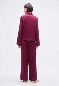 Ensemble de pyjama mauve comprenant un haut à manches longues avec boutons et col, et un pantalon à jambes larges, fabriqué en tissu léger avec une finition texturée.