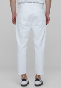 Valged teksapüksid sirge lõikega, viie taskuga ja siledast materjalist, kantud mustade ja valgete spordijalkadega.