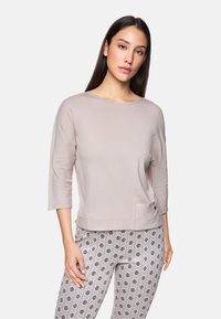Hellrosa, langärmliges Oberteil mit rundem Halsausschnitt und seitlicher Tasche; weicher Stoff mit glatter Textur. Kombiniert mit gemusterten Leggings.