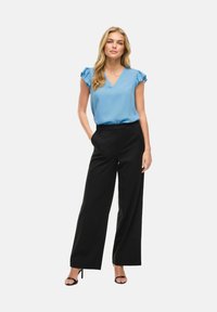 Gaiši zila īsām piedurknēm blūze ar volānu detaļām, apvienota ar melnām platām biksēm un melniem augstpapēžu sandalēm, veidojot elegantu look.