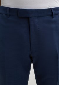 Dunkelblaue Hose mit einem subtilen strukturierten Muster. Verfügt über ein flaches Frontdesign, Gürtelschlaufen und eine taillierte Passform. Glatter Stoffabschluss.