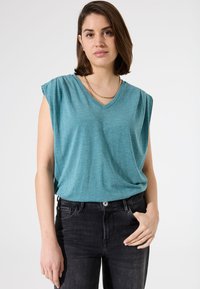 Türkisfarbenes V-Ausschnitt-T-Shirt mit Cap-Ärmeln, aus einem leichten Material gefertigt. Getragen mit schwarzen Jeans. Einfaches Design ohne sichtbare Muster.