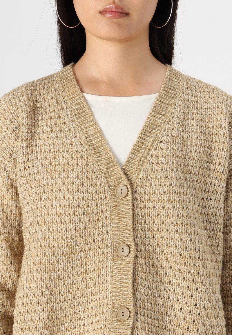 Cardigan en maille beige avec un col en V, présentant un motif texturé, cinq boutons et un bord côtes le long du col et de l'avant.