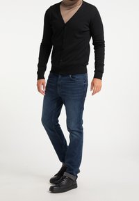 Cardigan nero con scollo a V e chiusura a bottone, abbinato a jeans in denim scuro e sneakers alte nere. Tessuto liscio, vestibilità casual.