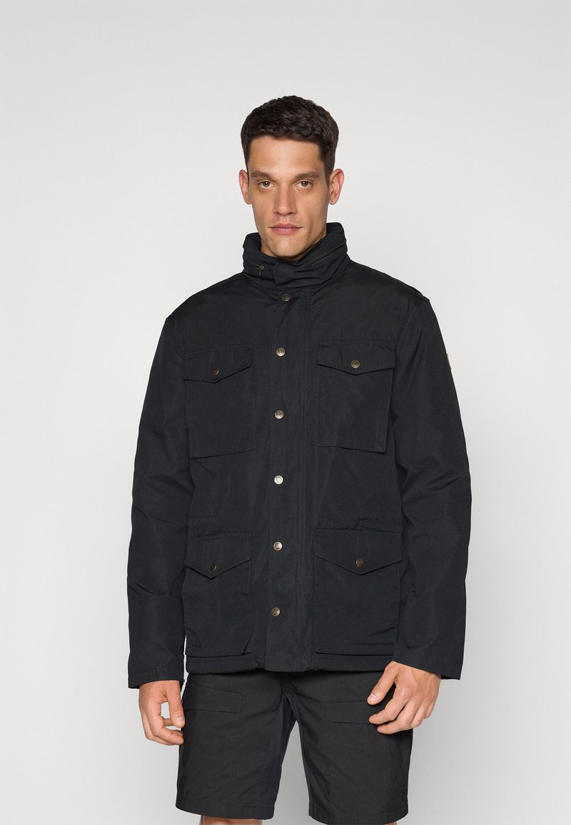 Black parka jacket with a high collar, snap button closure, four front pockets, and a textured fabric finish. Minimalist design.