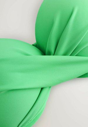 Close-up van een groene stoffen bikini top met gewatteerde cups en een brede band die over het midden loopt, plat gelegd op een lichte ondergrond.