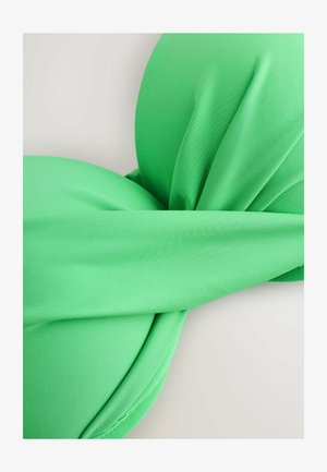 Zbliżenie na zielony materiałowy top od bikini z wyściełanymi miseczkami i szerokim paskiem przecinającym środek, położony płasko na jasnej powierzchni.