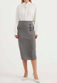 Weiße Bluse mit einem gerafften Ausschnitt und langen Ärmeln, kombiniert mit einem grauen Bleistiftrock mit Nadelstreifen, der eine Seitentasche und Knopfdetails hat.
