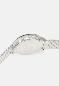 Orologio in acciaio inossidabile argento con cinturino a rete, dotato di cassa rotonda, corona e due pulsanti. Superficie liscia e lucida con dettagli incisi.