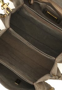 Interno di borsa in pelle scamosciata grigia con più scomparti, dettagli in metallo dorato e texture morbida. Presenta cuciture visibili e un'etichetta con marchio.