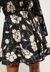 Rochie neagră cu un design floral în aurie și bej, având un material texturat, talie ajustată și fustă evazată cu accente intricate.