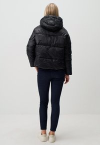 Zwarte pufferjack met capuchon, gewatteerd ontwerp en elastische manchetten. Gecombineerd met donkerblauwe slim-fit jeans en witte sneakers.